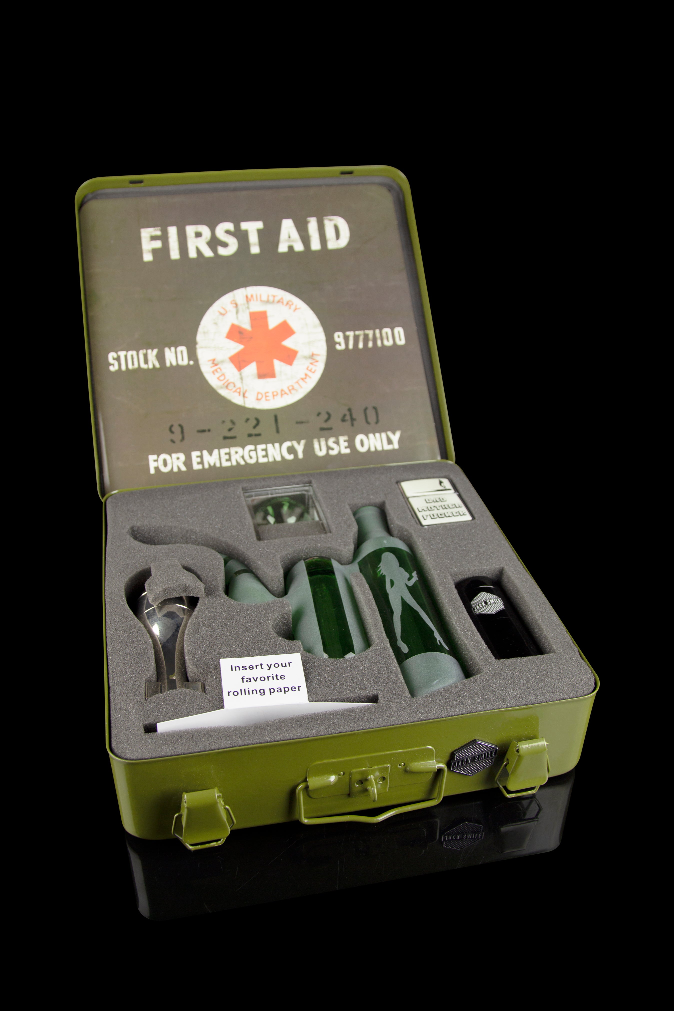 Vintage green first aid kit open to reveal cannabis smoking accessories including pipes, grinders, and rolling papers, displayed on black foam.