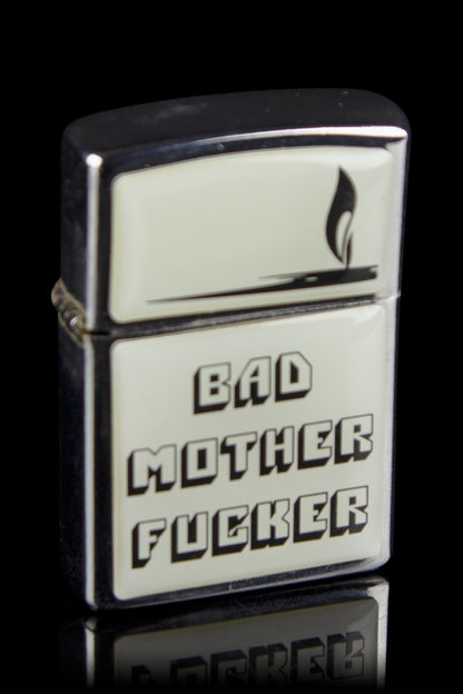 Silver Zippo lighter with bold black text reading “BAD MOTHER FUCKER” and a flame icon.