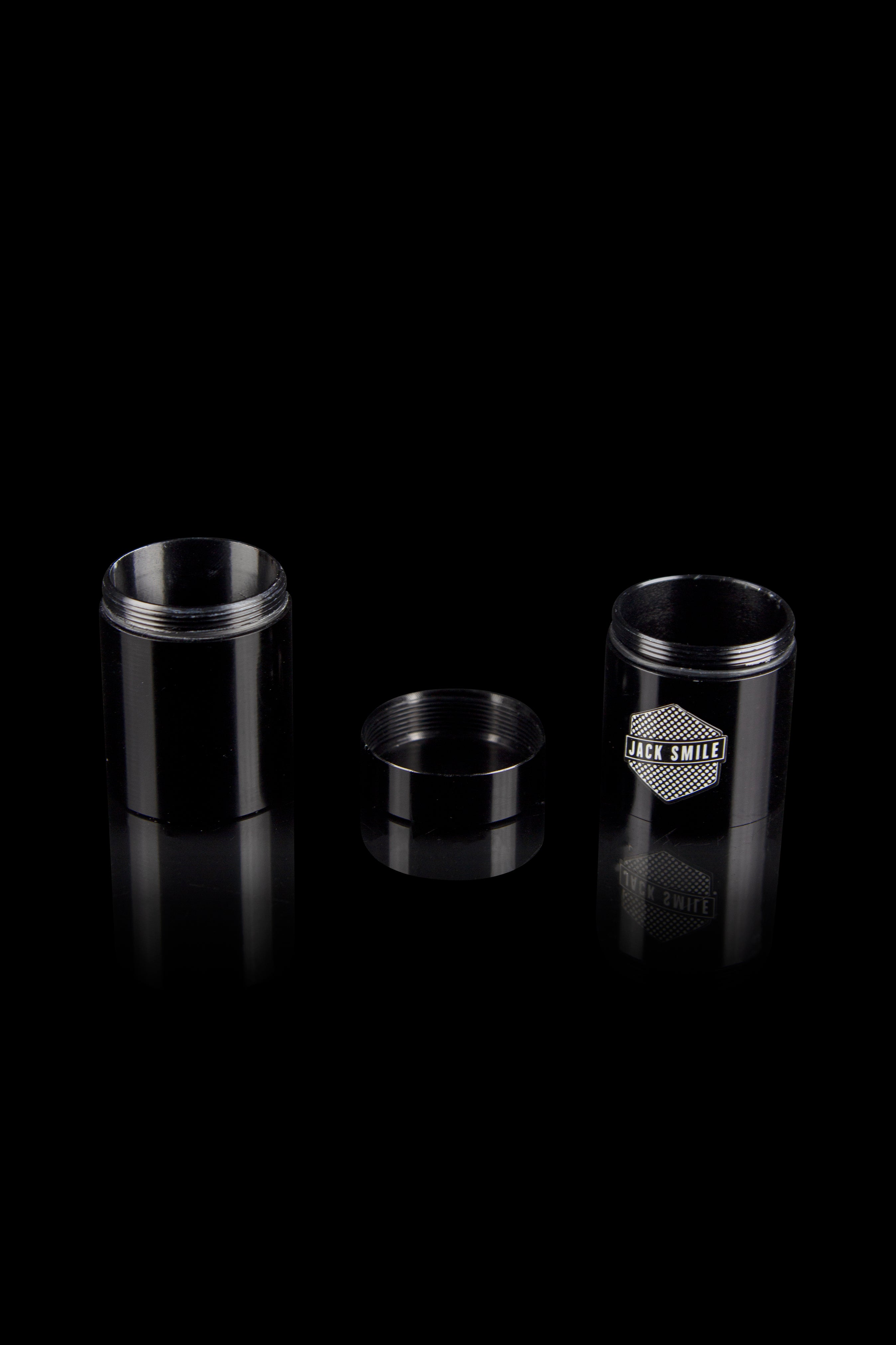 Black metal cannabis concentrate container with open and closed versions displayed, reflecting on a dark surface.