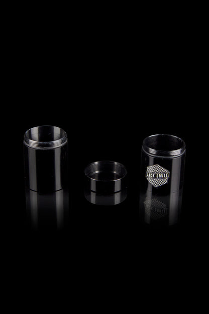Black metal cannabis concentrate container with open and closed versions displayed, reflecting on a dark surface.