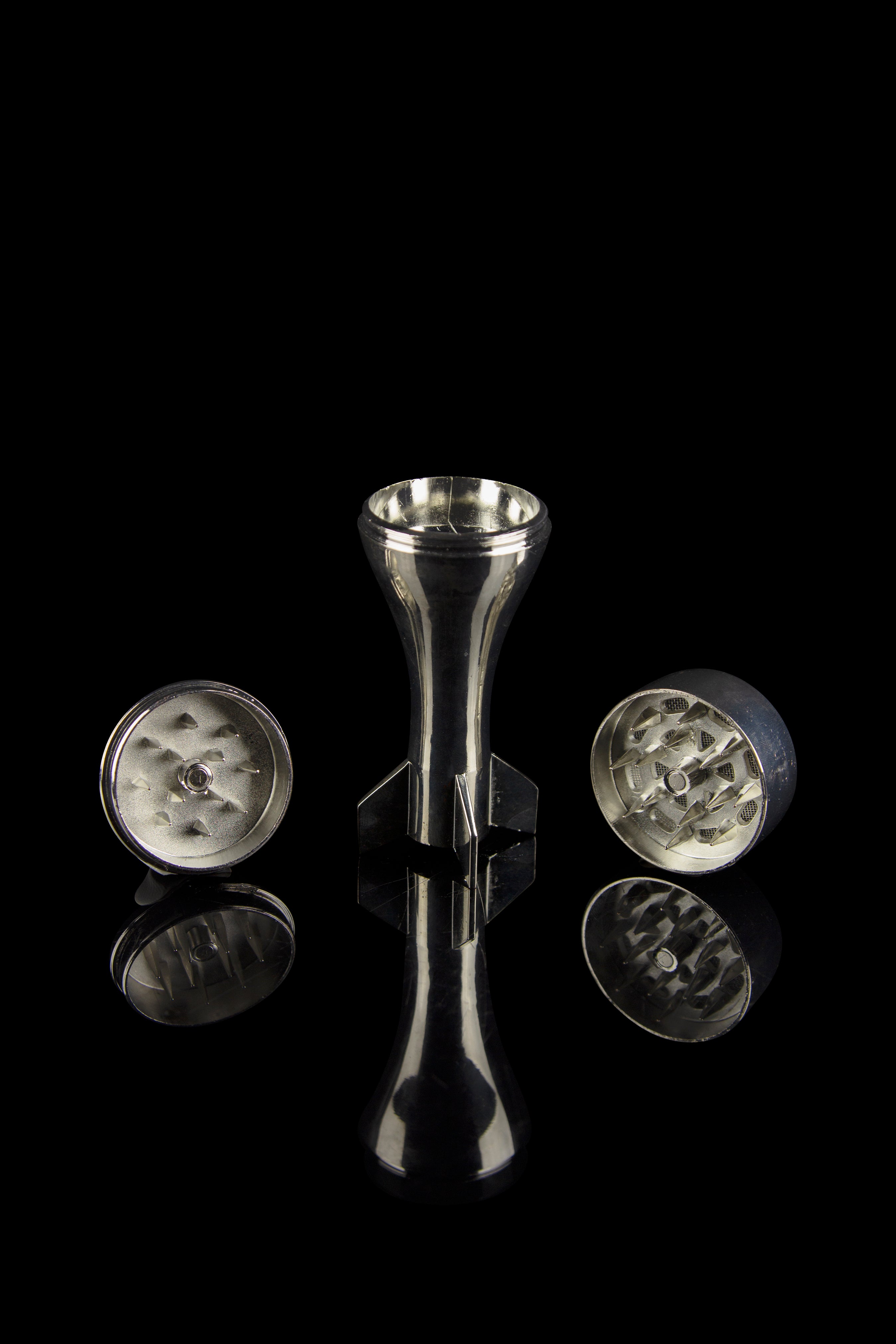 Silver cannabis grinder disassembled on a reflective black surface.