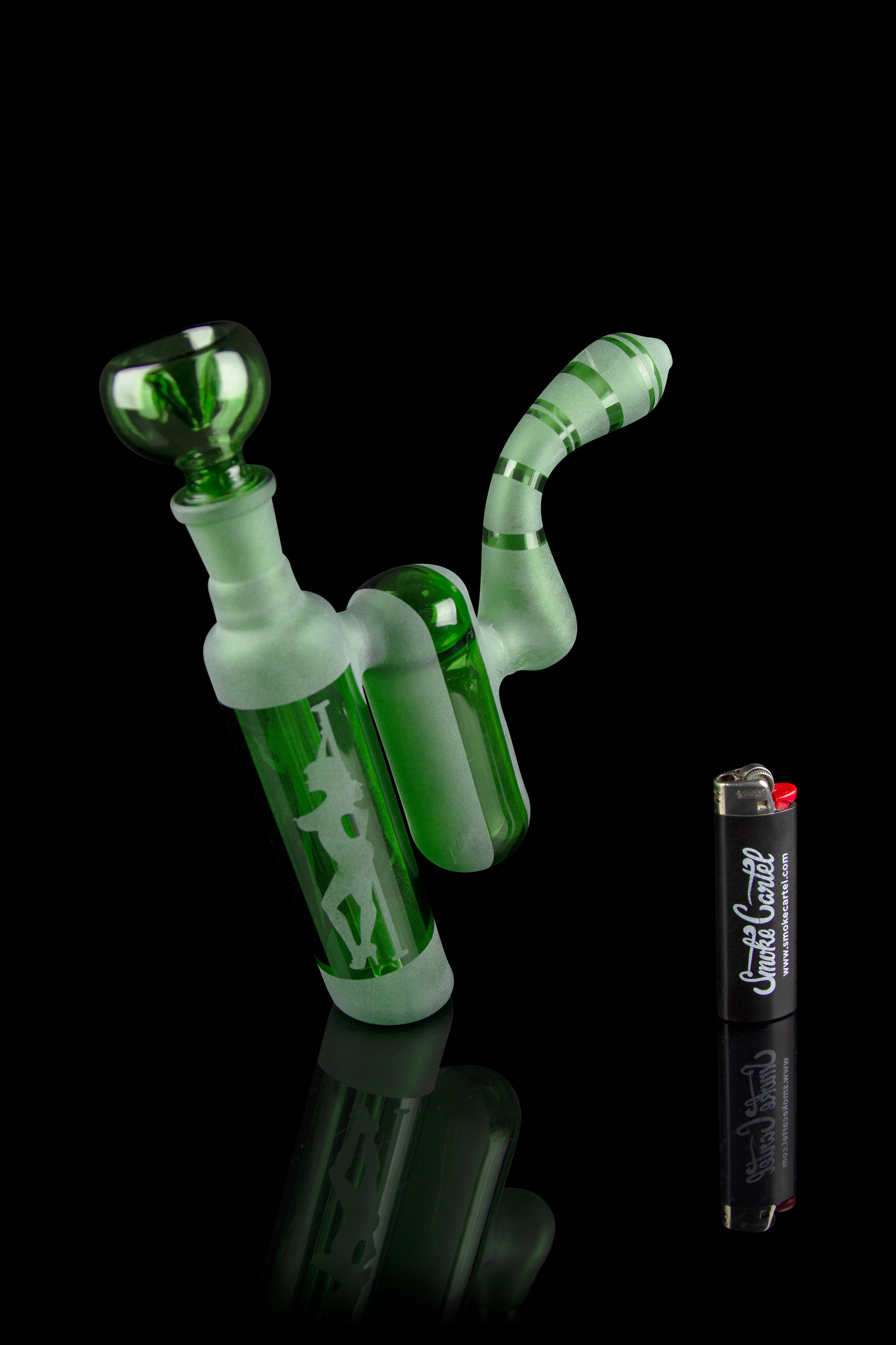 Glowing green glass bubbler pipe with a lighter and container on a dark background.