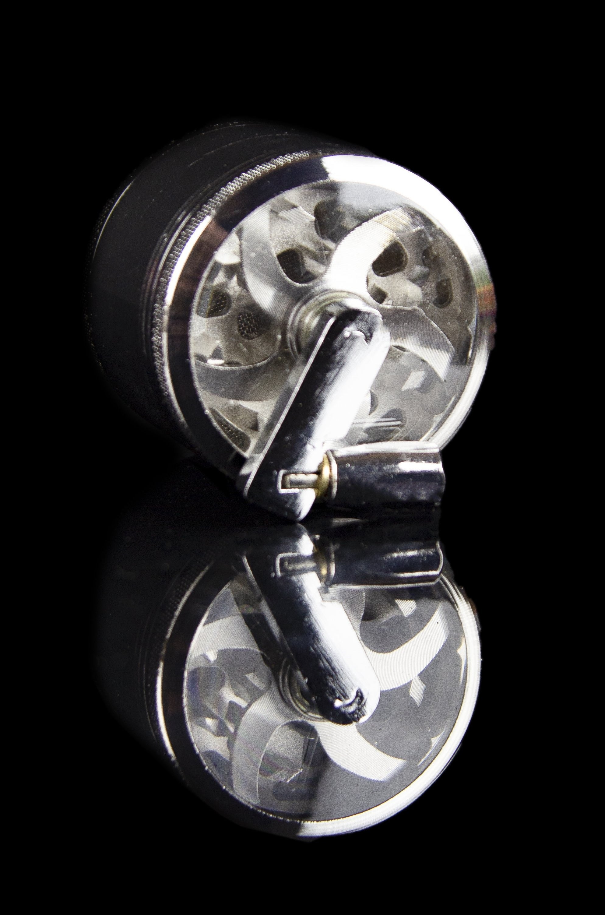 Silver and black cannabis grinder with a mirrored reflection on a black surface.