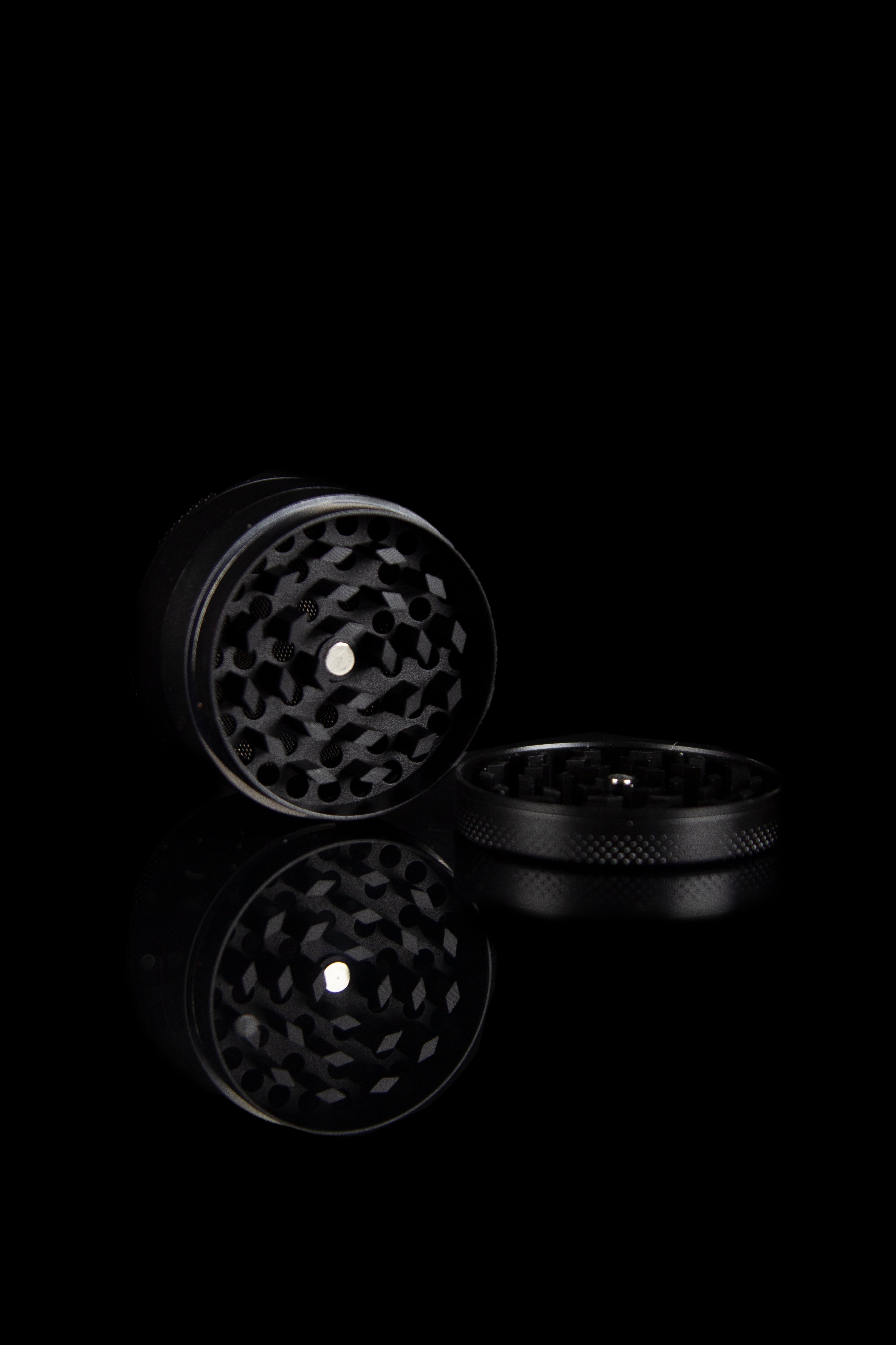 Black metal cannabis grinder, open, against a dark background.