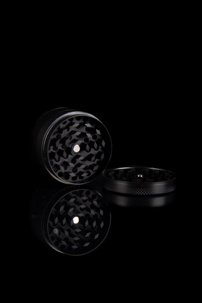 Black metal cannabis grinder, open, against a dark background.