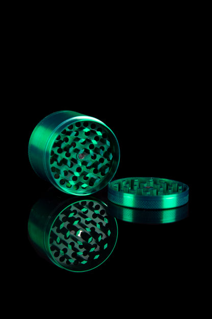 Green metal cannabis grinder disassembled on a black surface.