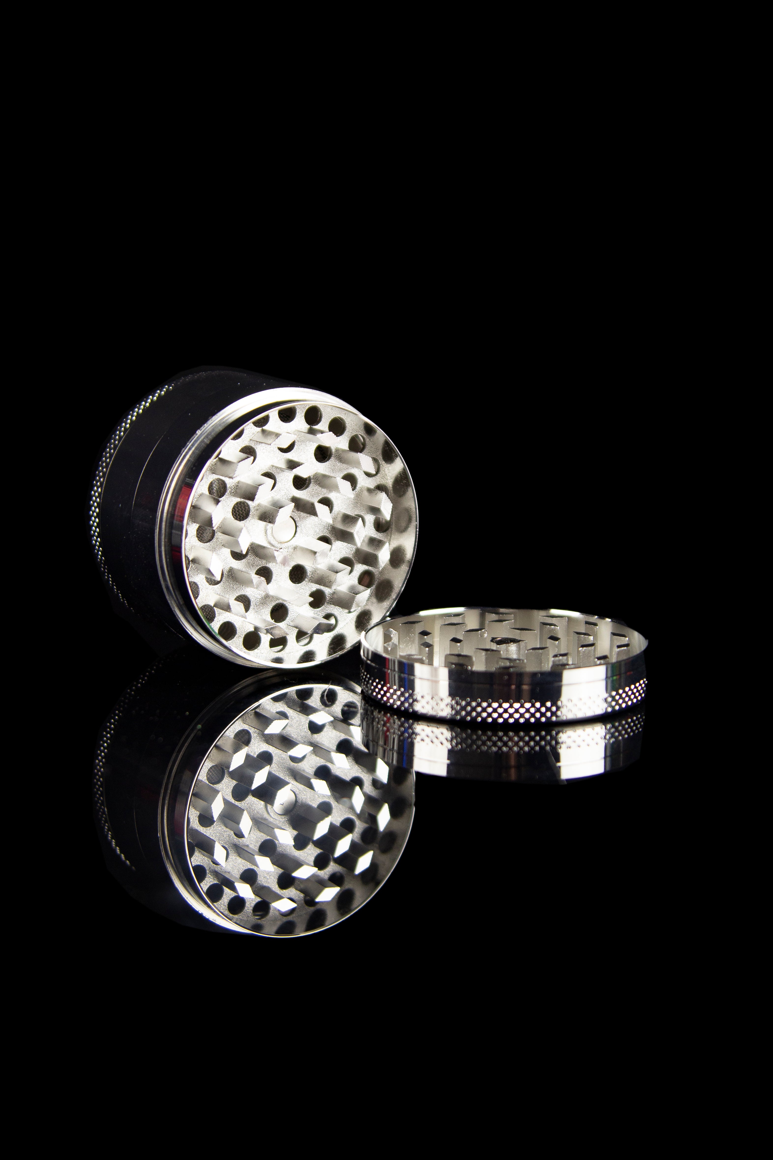 Silver cannabis grinder with open chambers, showcasing the grinding teeth and collection base, against a black background.