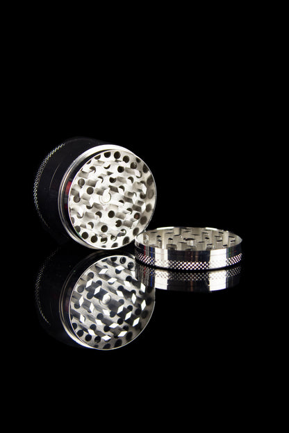 Silver cannabis grinder with open chambers, showcasing the grinding teeth and collection base, against a black background.