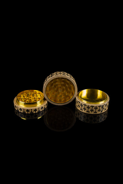 Gold cannabis grinder disassembled on a reflective black surface.