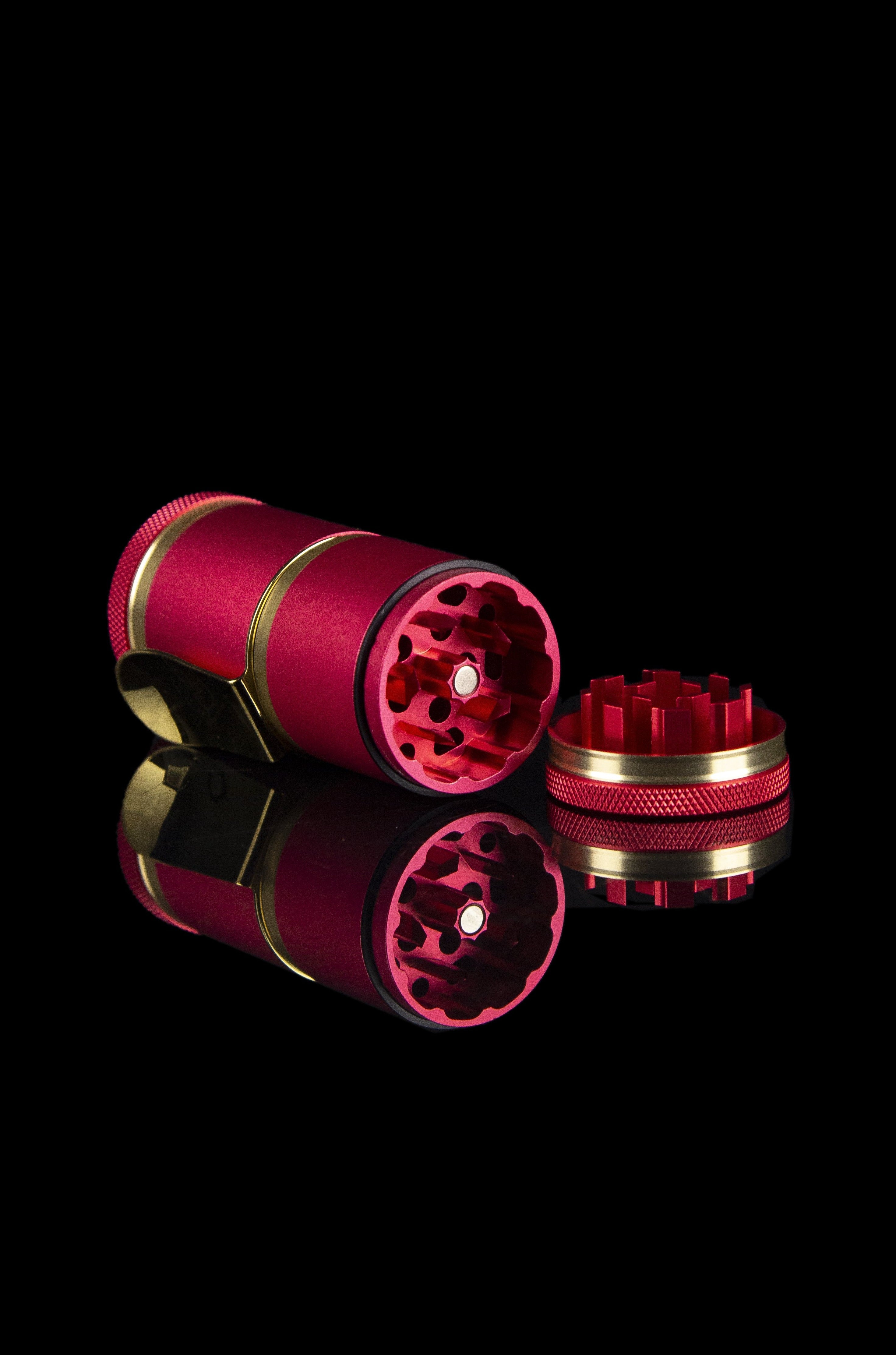 Pink and gold cannabis grinder with disassembled parts and a glossy reflection on a black background.
