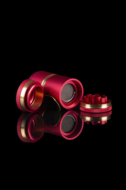 A disassembled, metallic pink and gold cannabis grinder with a reflective black surface.