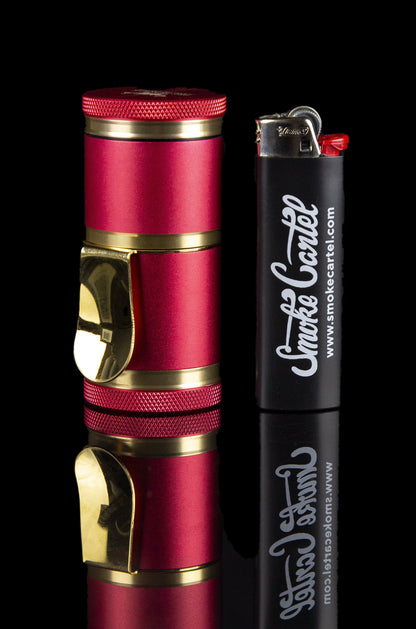 A shiny, crimson-colored grinder and lighter with “Smoke Cartel” branding reflected on a glossy black surface.