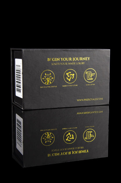 Two black boxes stacked on a dark surface, branded with gold foil text and icons promoting a cannabis lifestyle—"Begin Your Journey, Ignite Your Inner Luxury"—and a website address.