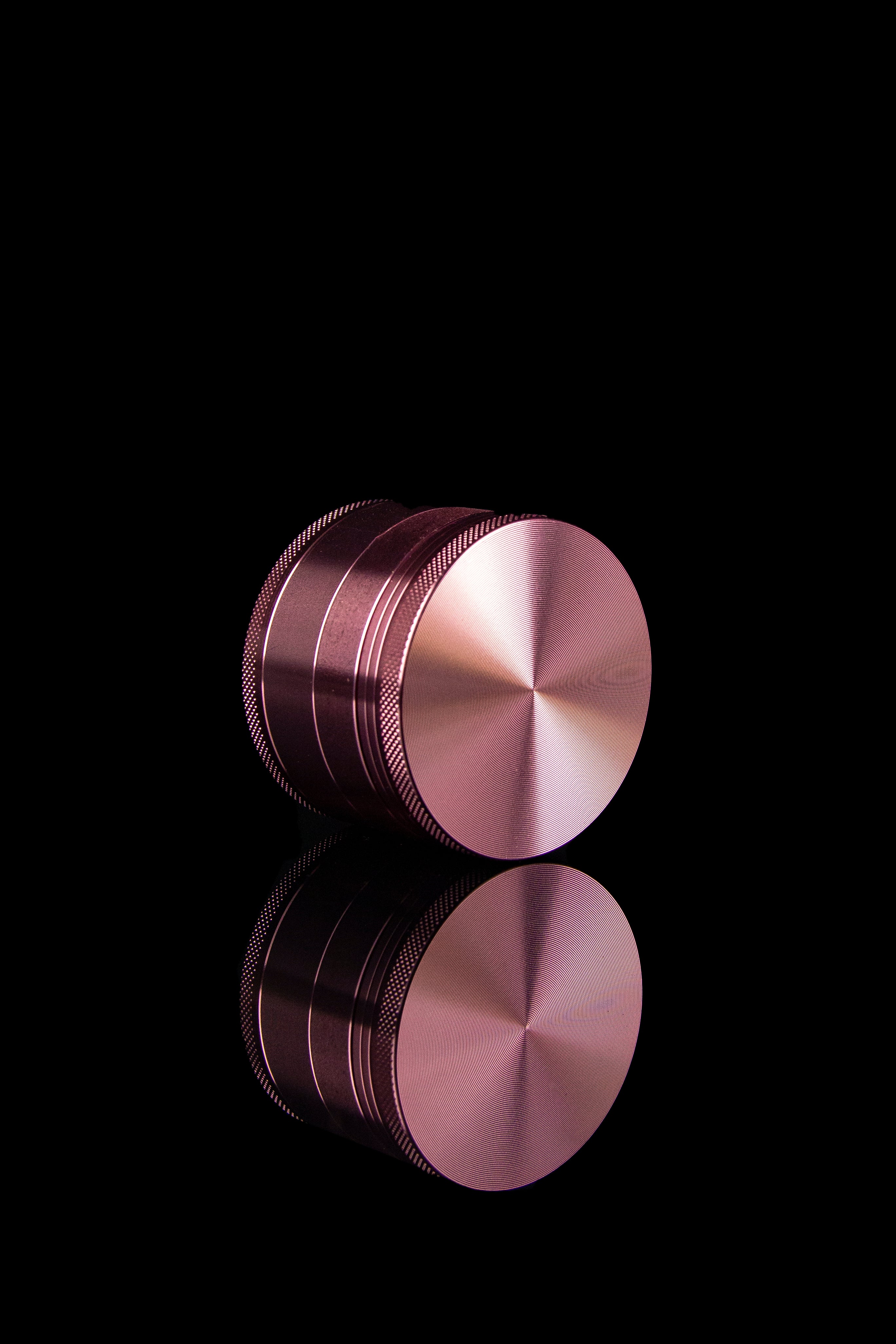 Rose gold cannabis grinder with reflection on black background.
