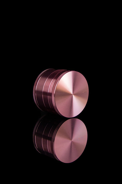 Rose gold cannabis grinder with reflection on black background.