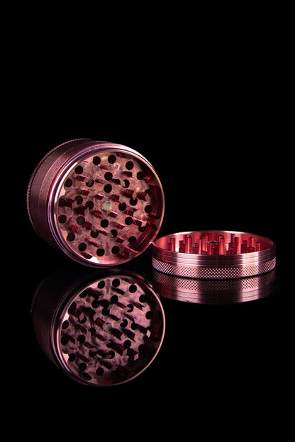 A disassembled, metallic cannabis grinder with visible grinding teeth, against a black background.