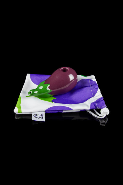 Purple glass pipe resting on a drawstring bag with a cartoon chameleon print and “Art of Smoke” logo, against a black background.