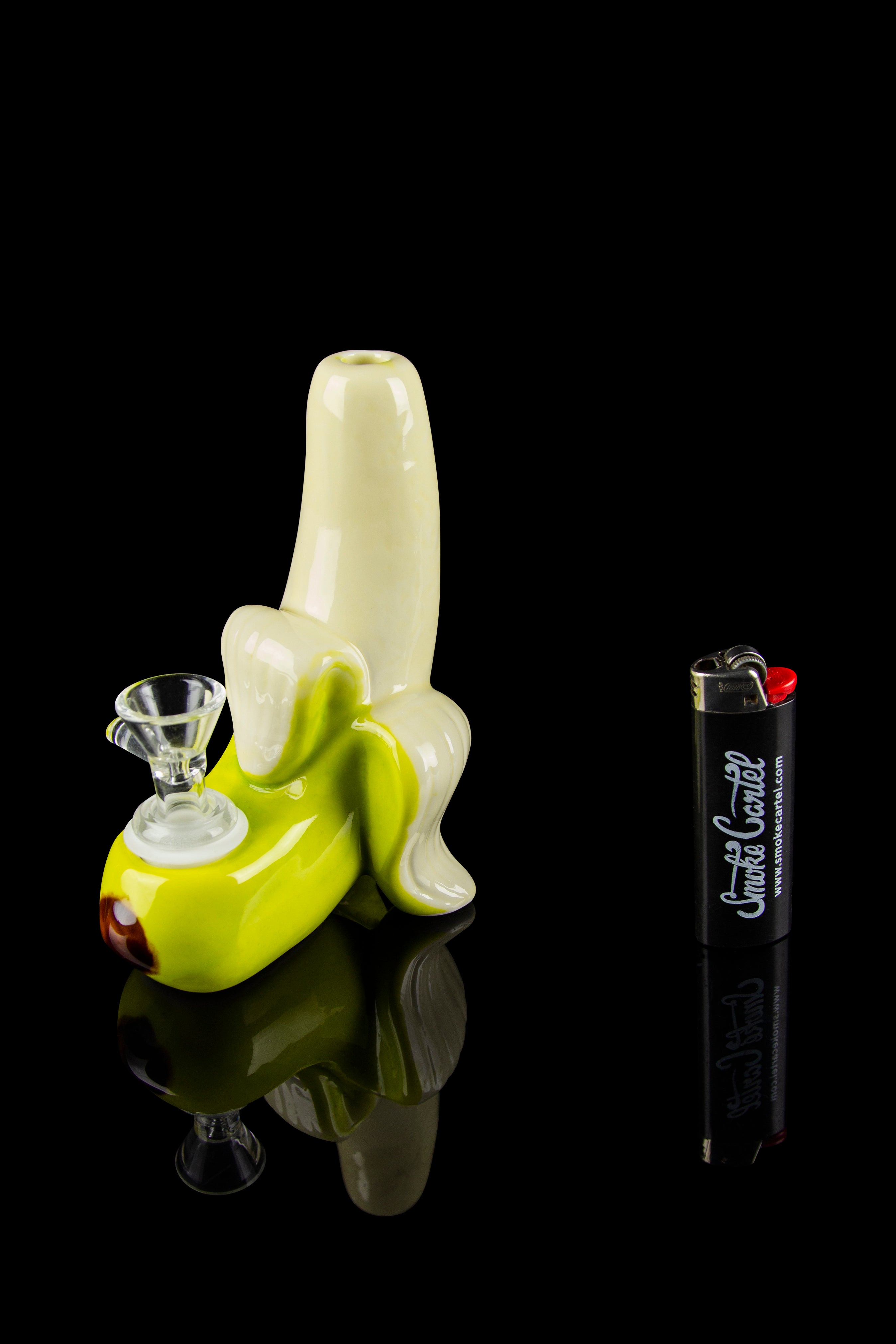 Green glass water pipe shaped like a middle finger, with a glass bowl and lighter beside it, reflected on a shiny black surface.