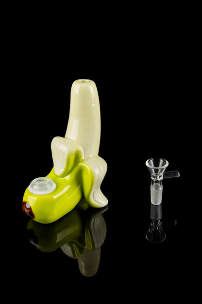 Glass banana-shaped water pipe and accompanying glass bowl, displayed on a reflective black surface.