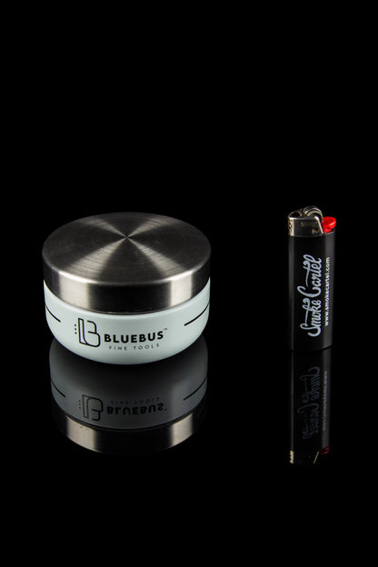 Sleek silver cannabis storage jar with a branded lighter on a black reflective surface.