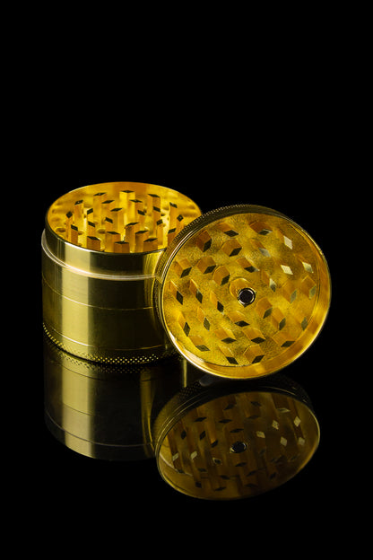 Gold cannabis grinder with open chambers and reflective surface, isolated on black.