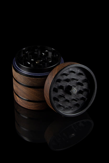 Open cannabis grinder with wooden and metal components, displayed against a dark, reflective background.