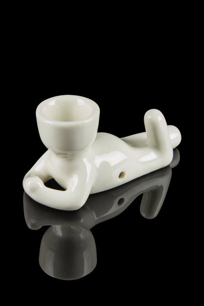 White ceramic chillum pipe shaped like a lounging figure, reflected on a black surface.