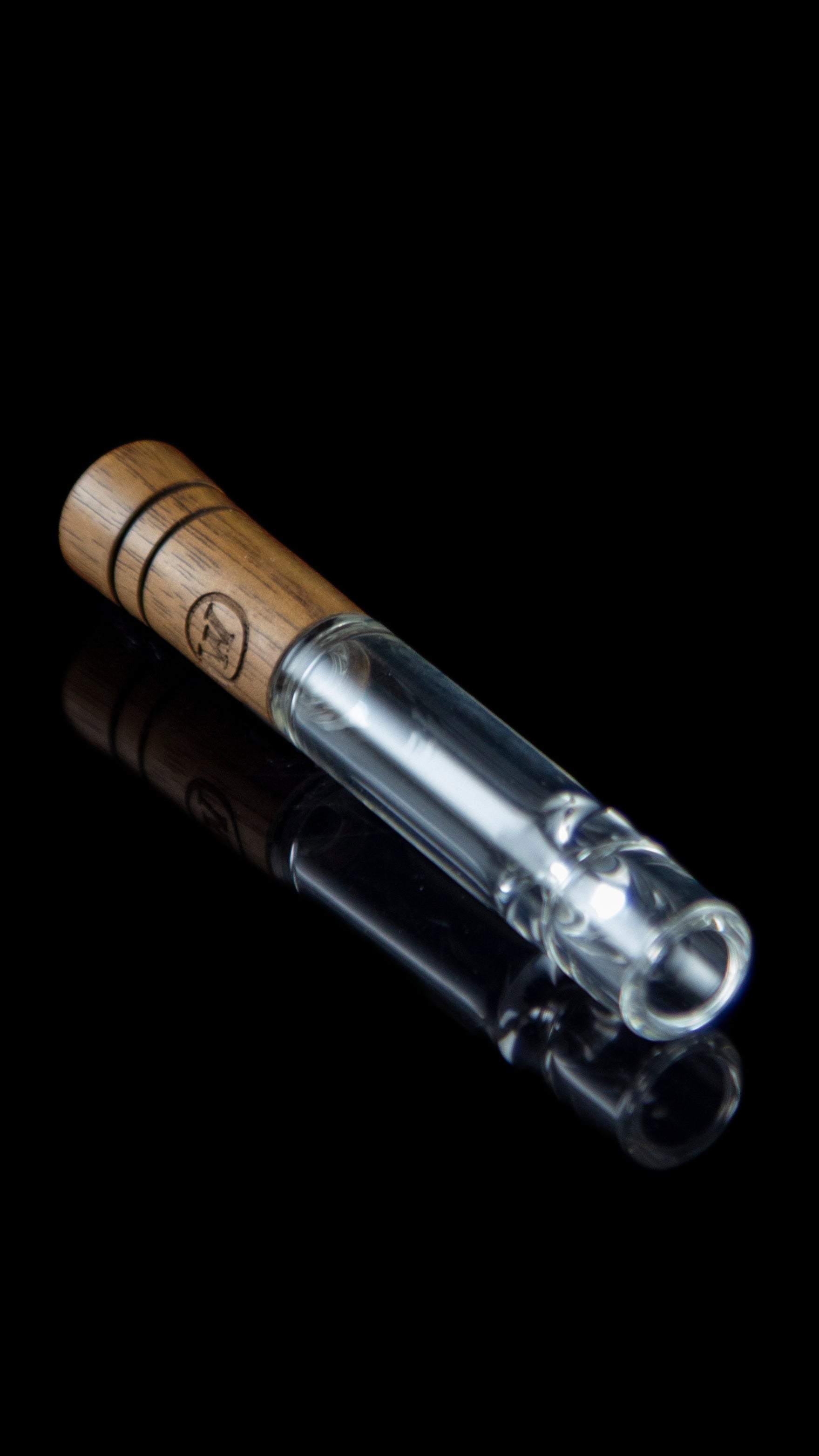 Glass pipe with wooden mouthpiece on a reflective surface.