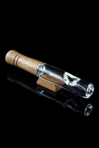 Glass bubbler pipe with a wooden mouthpiece, reflecting on a glossy black surface.