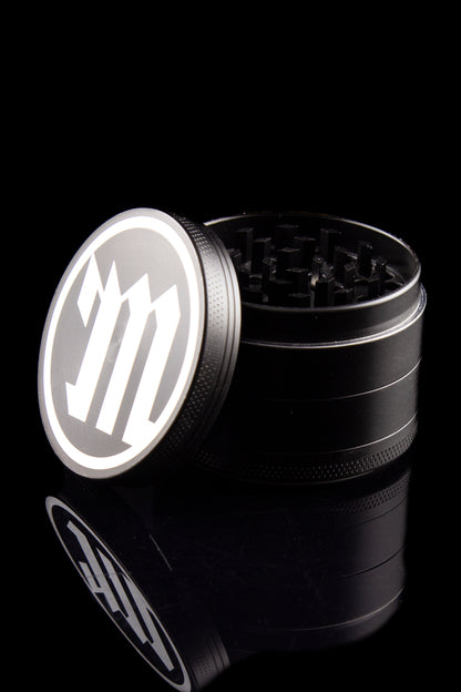 Black metal cannabis grinder with a branded lid, partially disassembled, against a dark reflective surface.