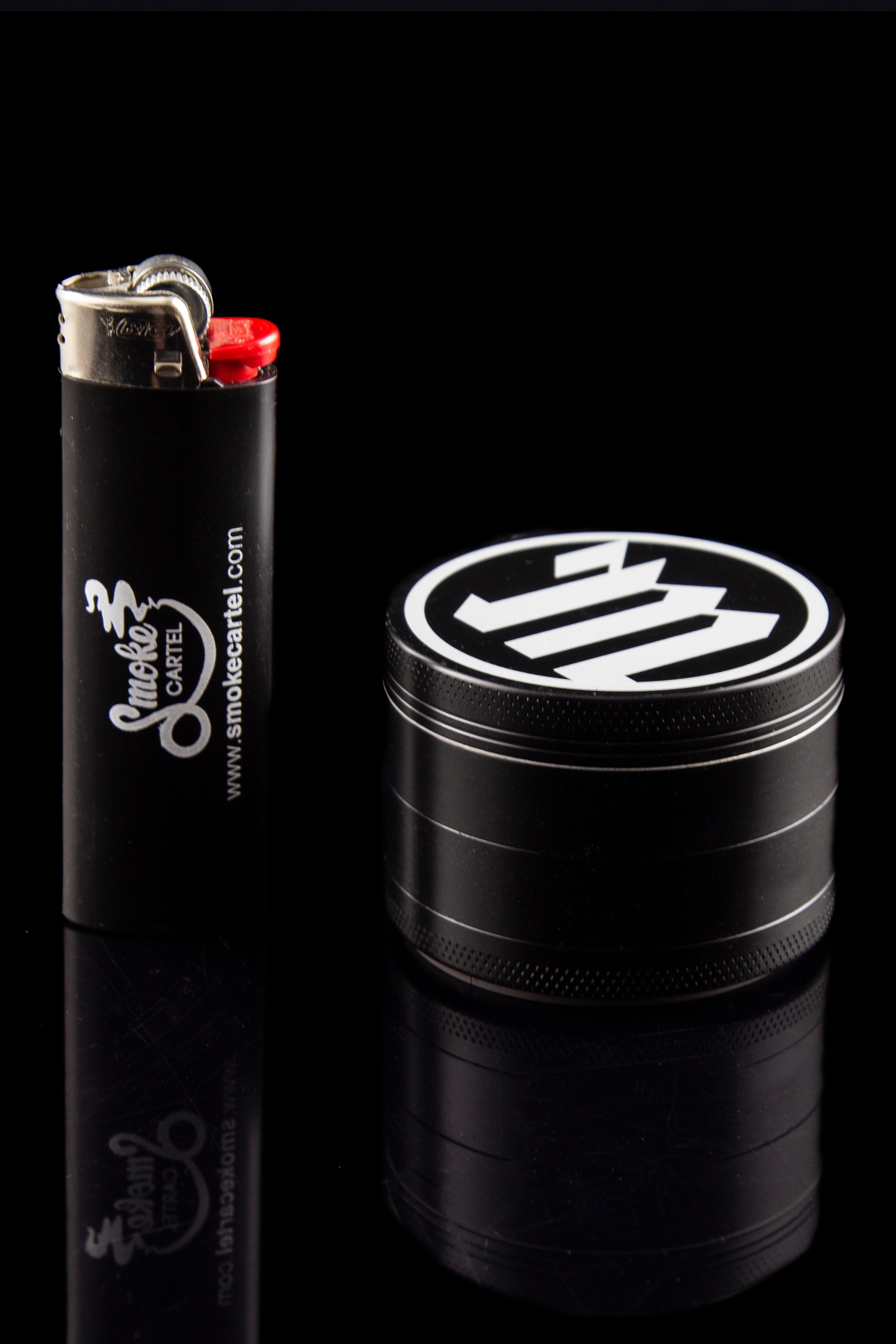 Black grinder and lighter with "Smoke Cartel" branding on a reflective surface.