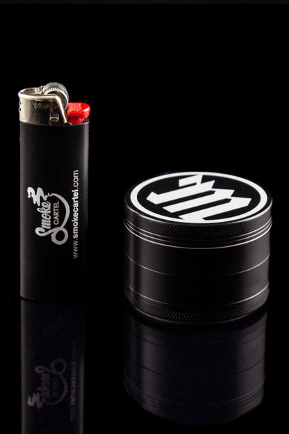 Black grinder and lighter with "Smoke Cartel" branding on a reflective surface.
