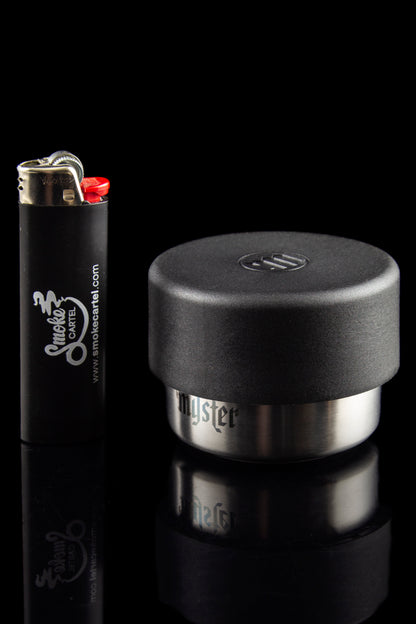 Black cannabis storage jar and lighter with branding for Smoke Cartel, reflecting on a glossy surface.