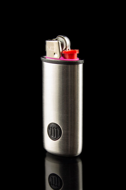 Silver cannabis grinder with a lighter inserted into the top, reflecting on a black surface.