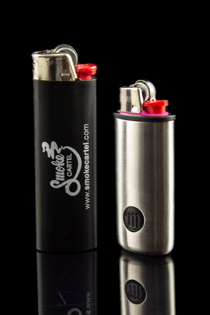Two butane lighters with branding for Smoke Cartel, displayed on a reflective black surface.