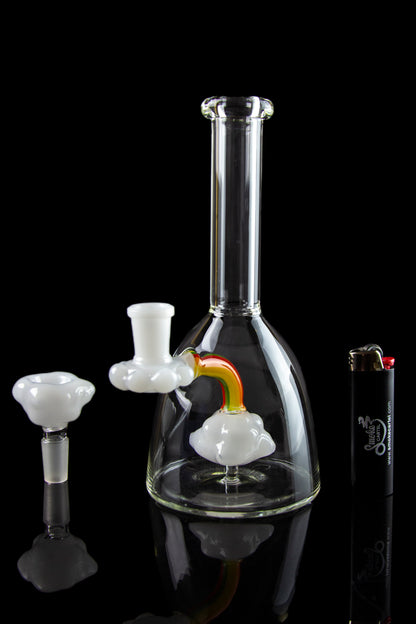 Clear glass water pipe (bong) with colorful attachments, displayed on a reflective surface against a black background.