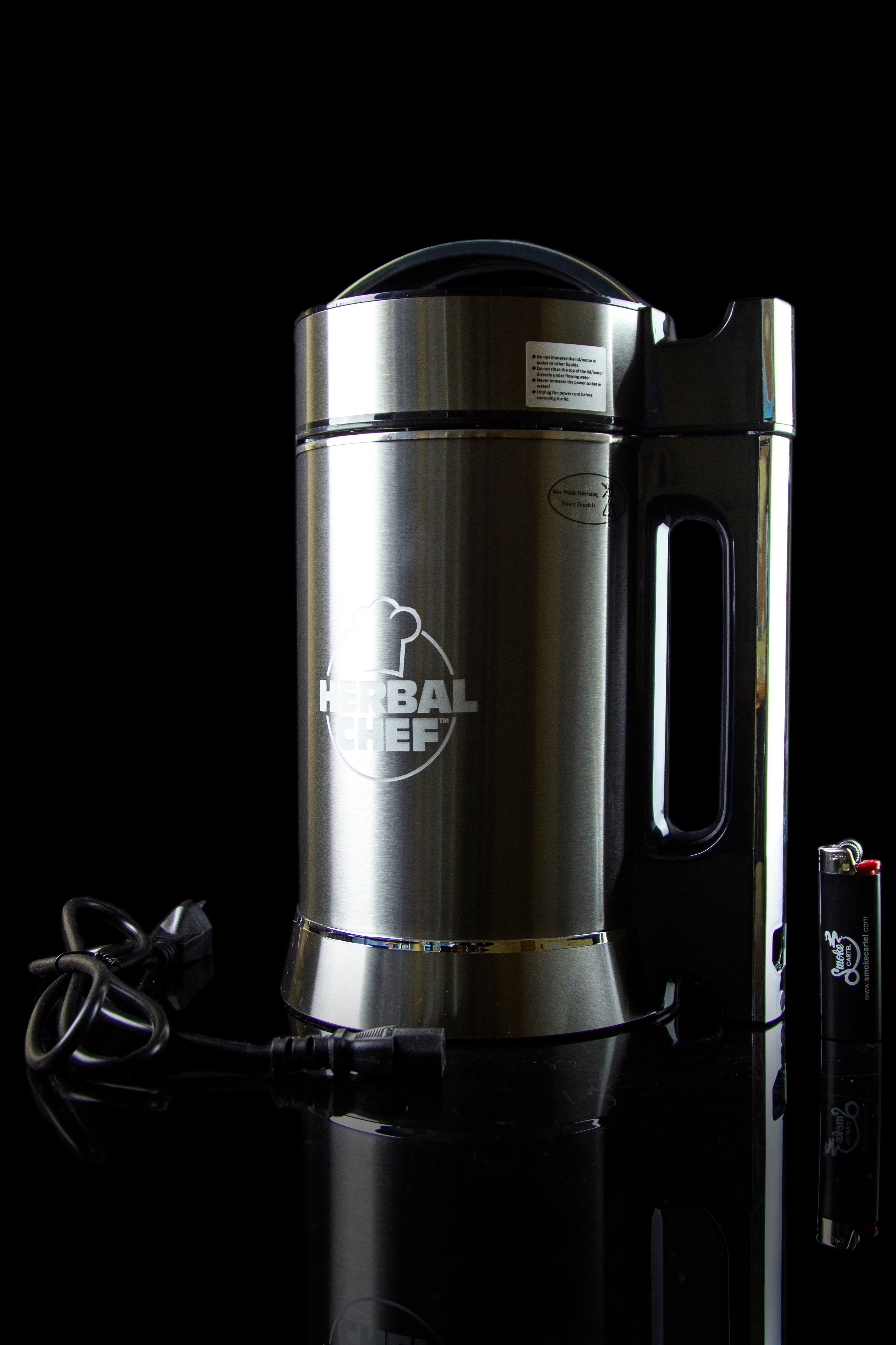 Stainless steel Herbal Chef infusion appliance with power cord and lighter on a reflective black surface.