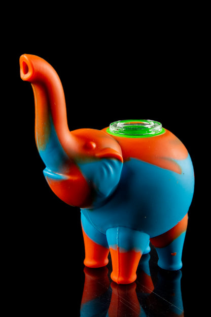 A front view of the Silicone Elephant Bubbler Pipe - Ellie, showcasing its colorful, sculpted form reflecting on a glossy surface.