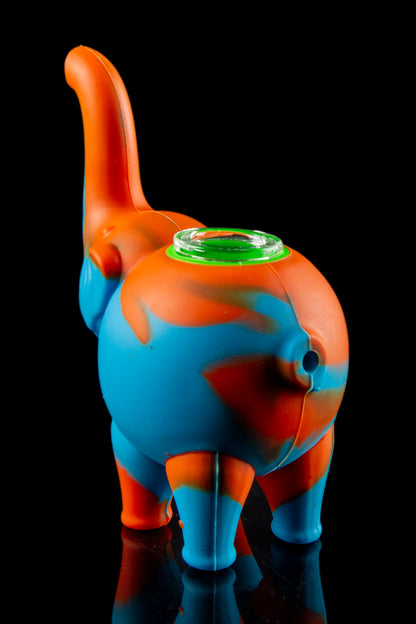 Silicone water pipe shaped like a cartoon elephant with orange and blue coloring, reflecting on a black surface.