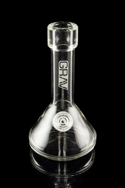 Clear glass water pipe (bong) with “GRAV” logo and ice pinch, reflecting on a black surface.