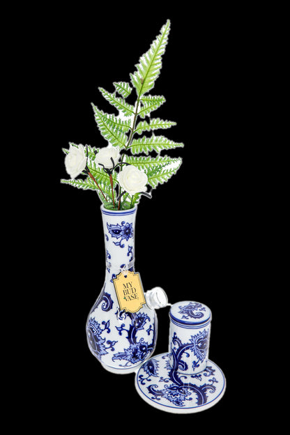 Blue and white porcelain cannabis vase with ferns and a matching jar and saucer, against a black background."