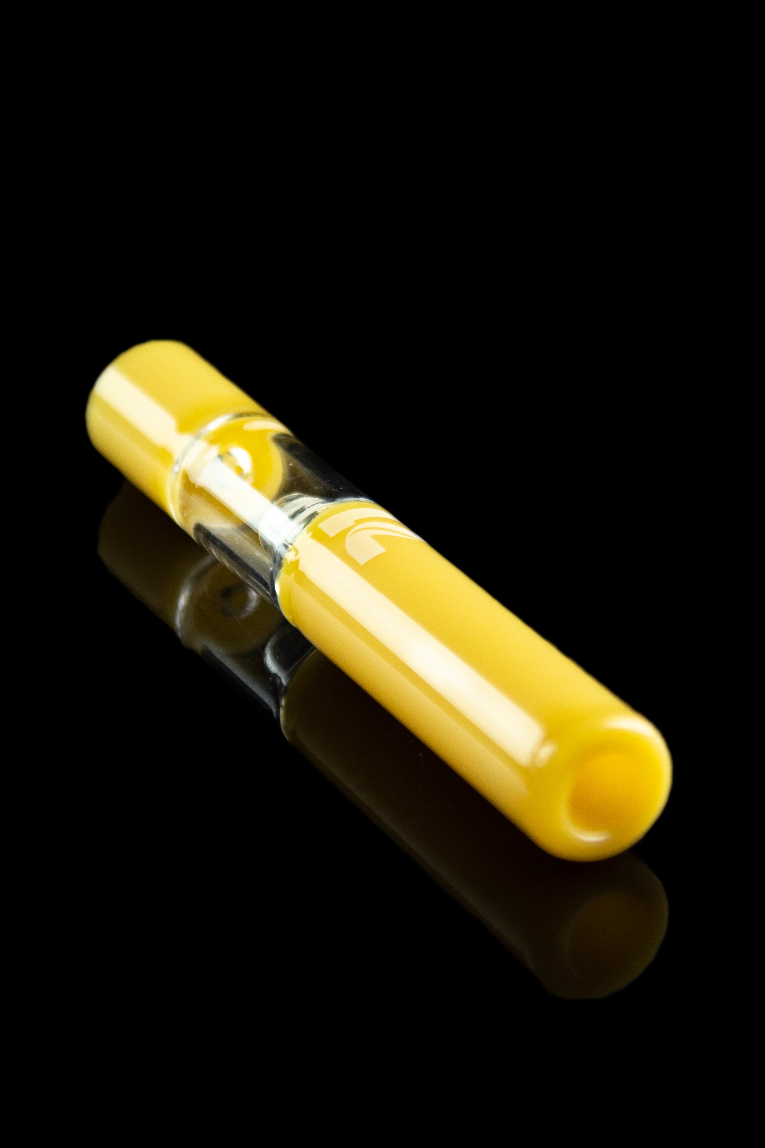 Yellow glass cannabis oil burner pipe with a clear glass bubble, reflecting on a black surface.
