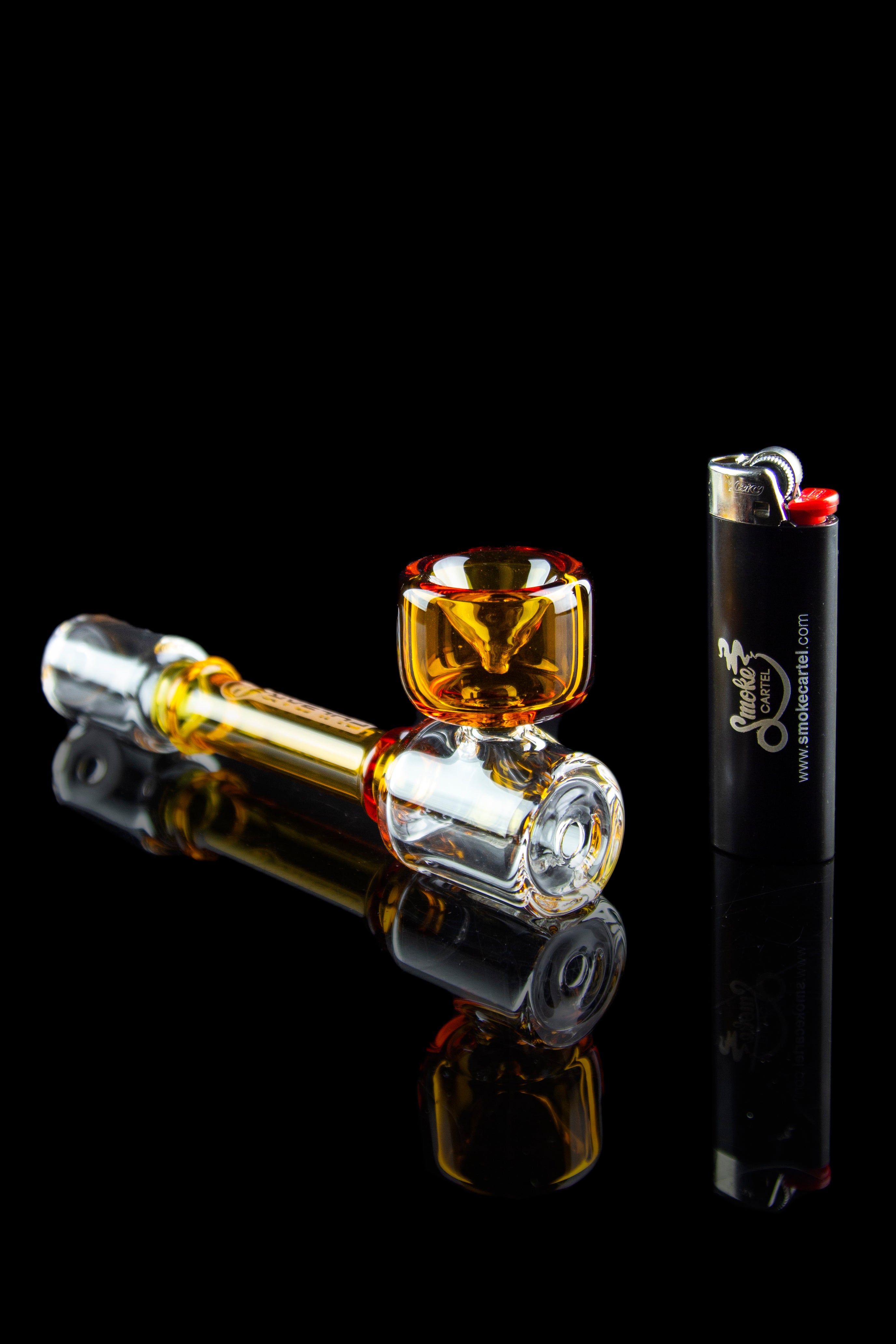 Glass cannabis pipe and lighter on a reflective black surface.