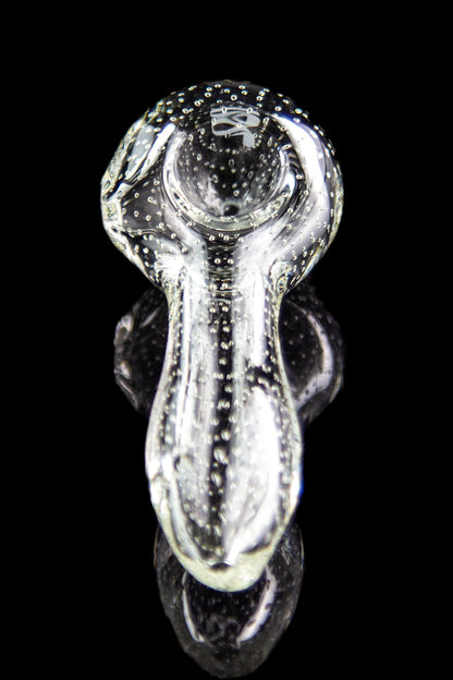 Clear glass bubbler pipe with speckled pattern, reflecting on a dark surface.
