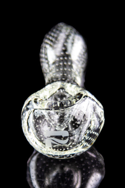 Clear glass cannabis oil rig with intricate bubble and swirl patterns, reflected on a black surface.