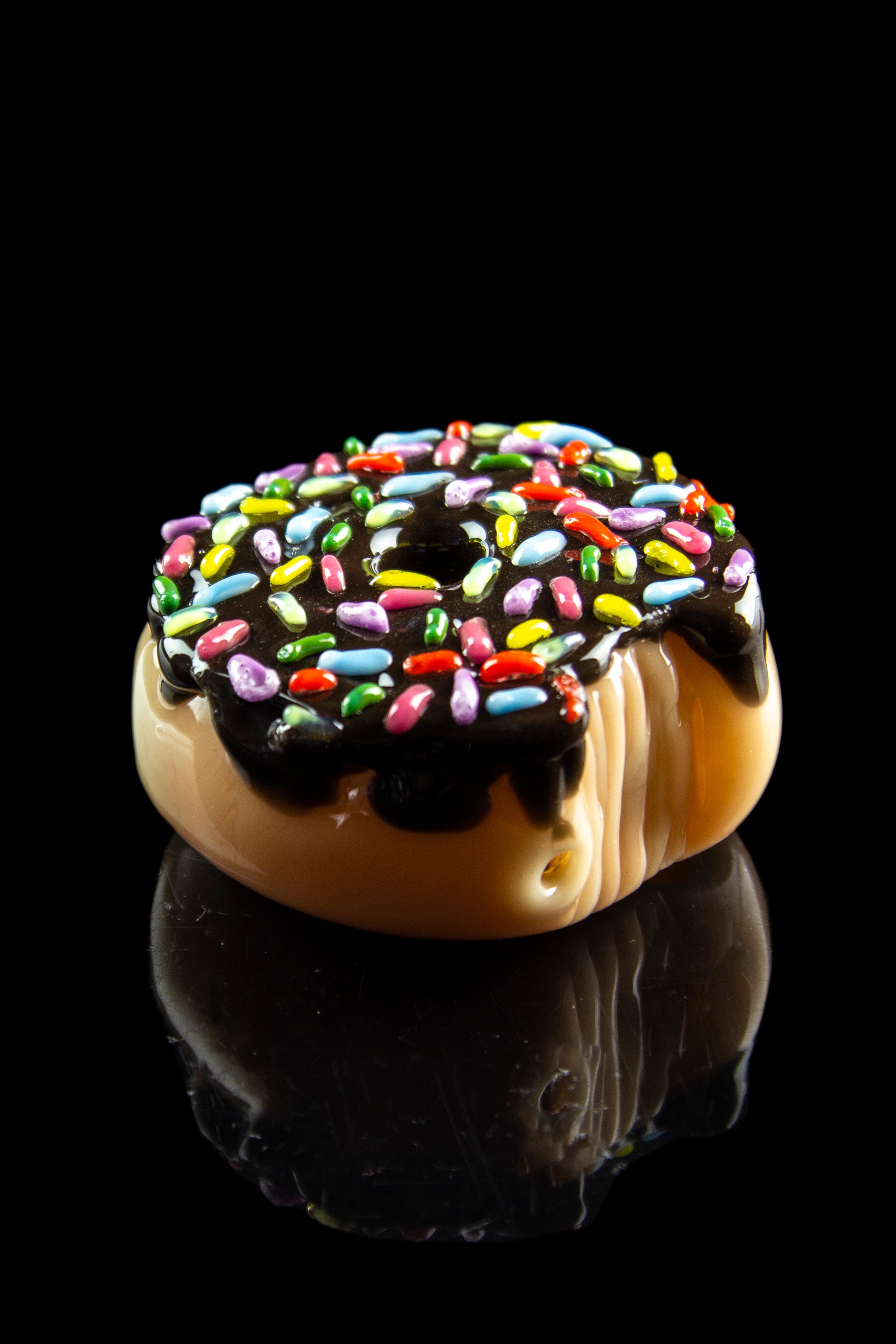 Glass pipe shaped like a sprinkled donut, reflecting on a black surface.
