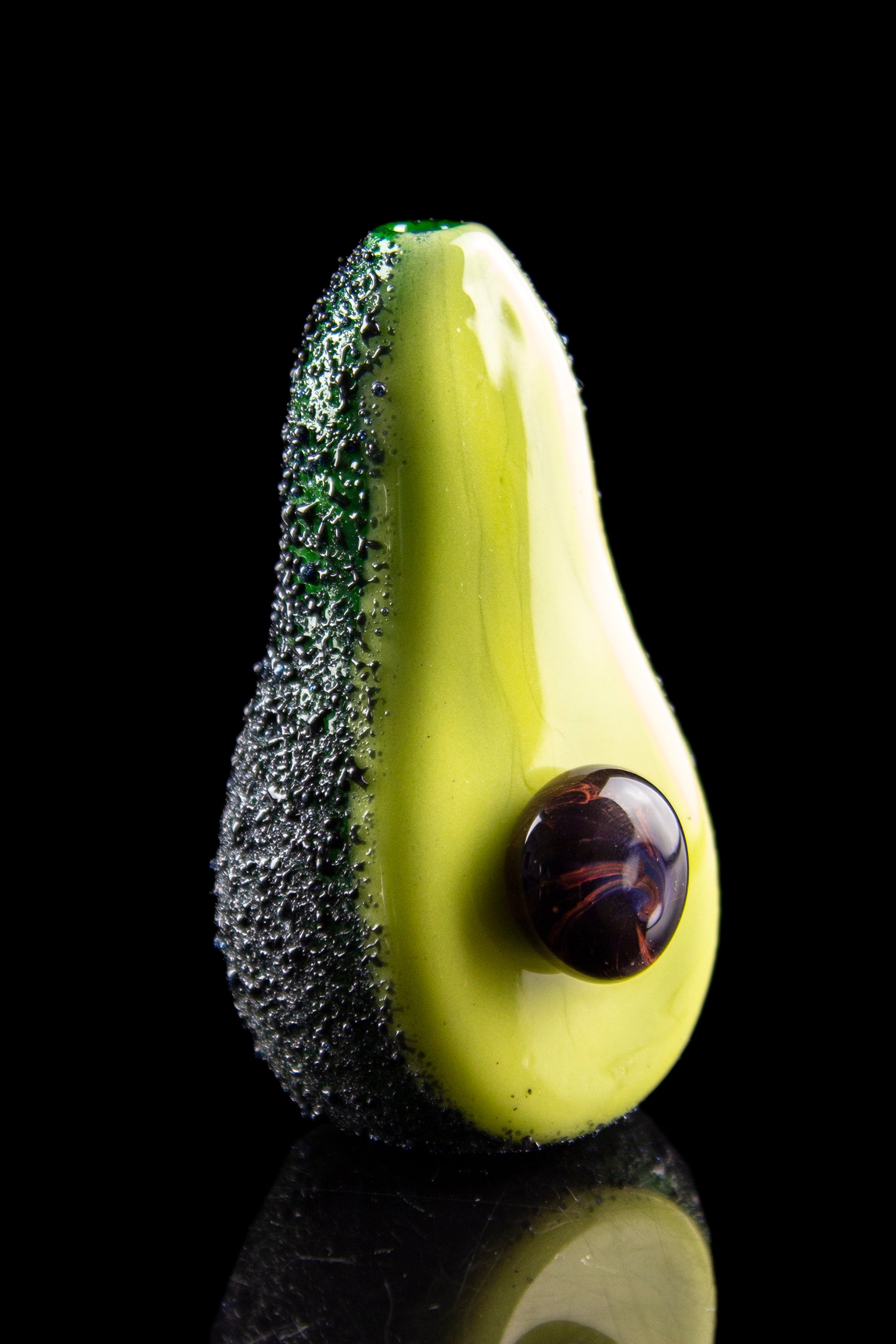 Glass avocado-shaped pipe with a dark, marbled sphere as the bowl, reflecting on a glossy black surface.