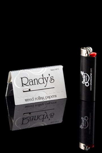 Pack of Randy's rolling papers and a black lighter with branding, reflected on a glossy surface. - Randy's Classic Wired Rolling Papers