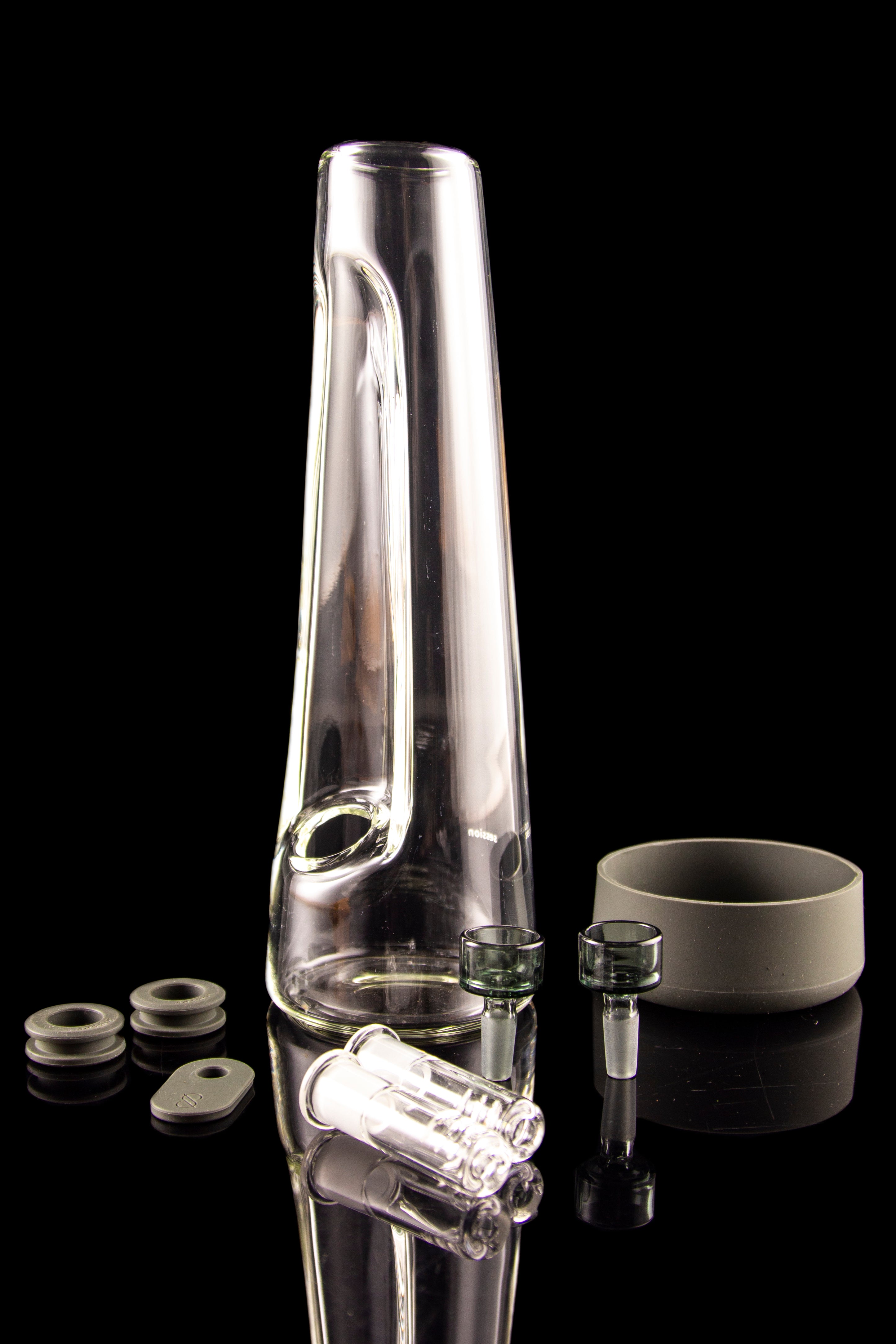 Clear glass bong with various attachments and components displayed on a reflective black surface.