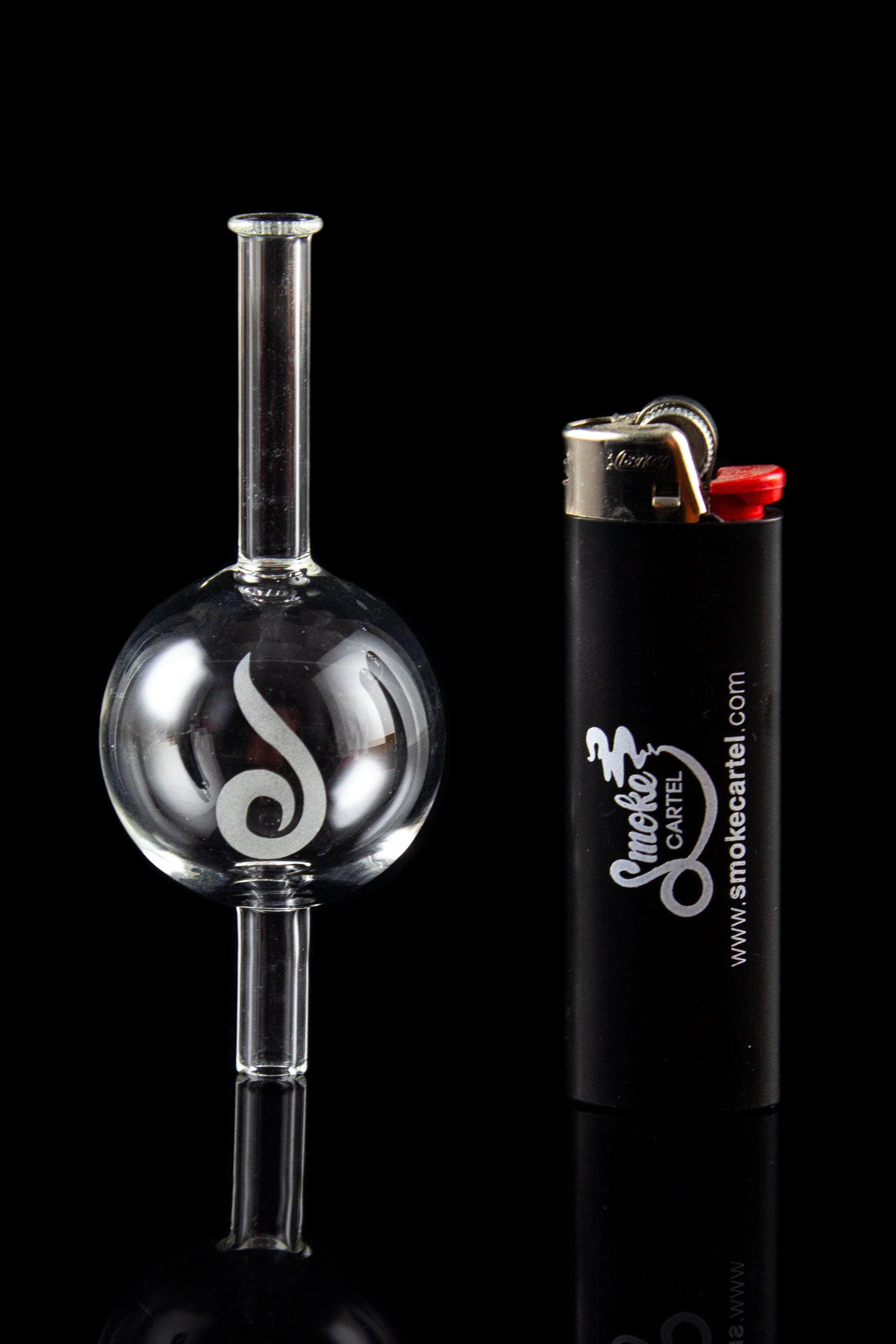 Glass oil rig with intricate design next to a lighter, reflecting on a glossy black surface.